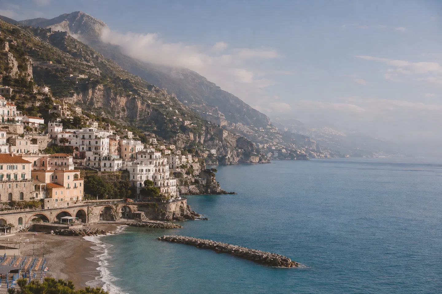 An Italian cliffside village curves around a quiet turquoise Mediterranean bay