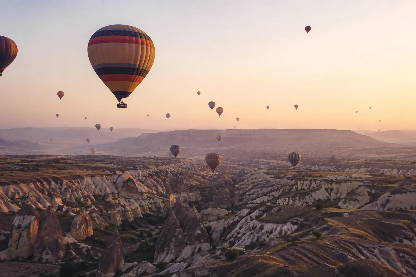 Hot-air balloons drift above Cappadocia’s sculpted rock valleys at dawn