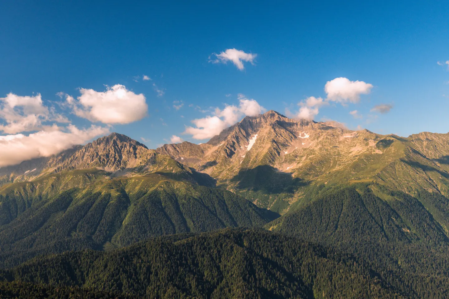 Sunlit Caucasus peaks and green forested slopes in the mountains above Sochi